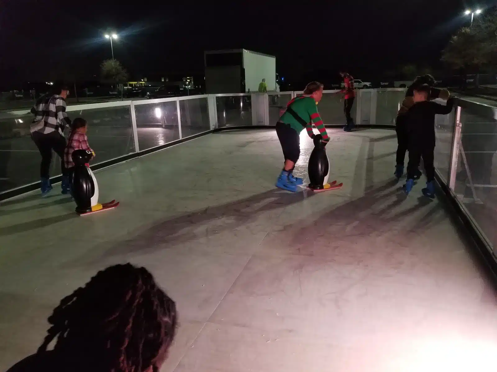 Guests learning to skate with penguin skate helpers on an illuminated synthetic rink